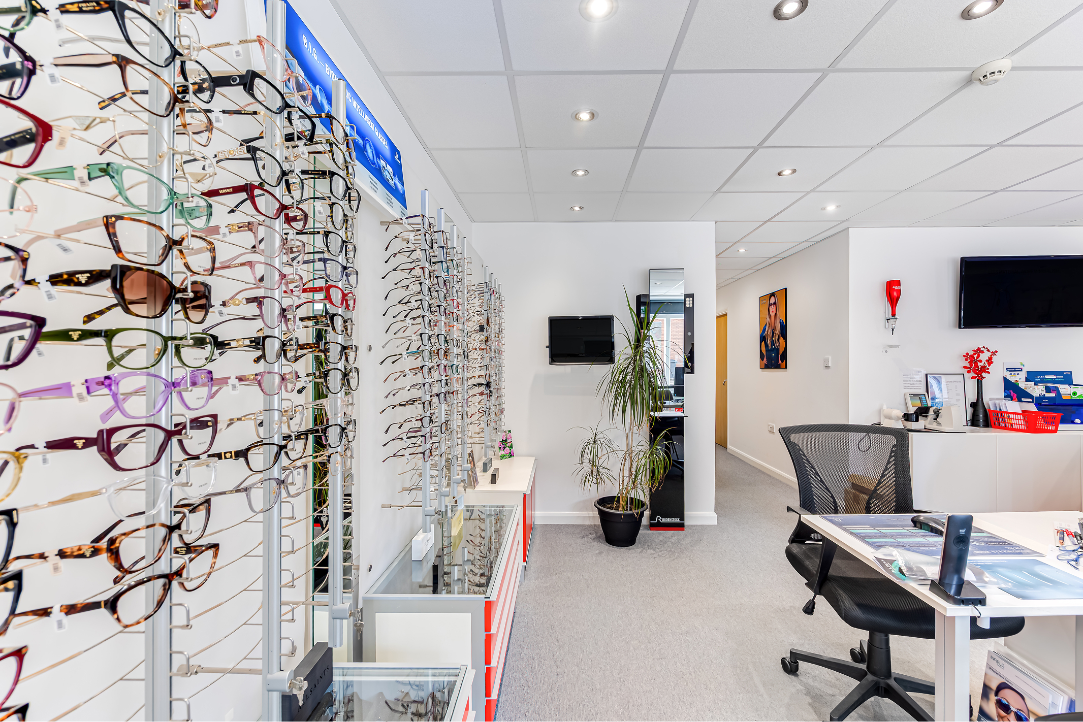 Optical store interior with large display of colorful eyeglasses, office desk, and modern ceiling