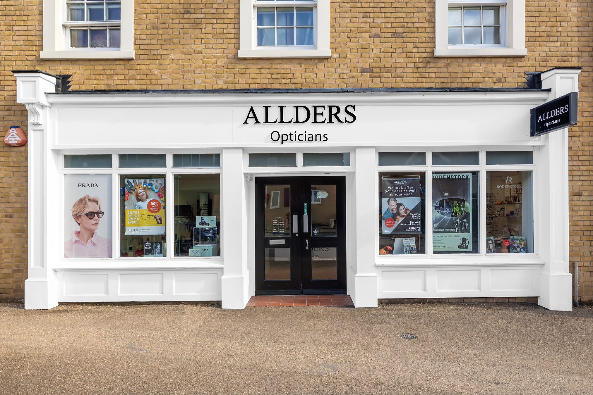 Allders Opticians storefront with white facade, brick building above, and display windows showing eyewear.