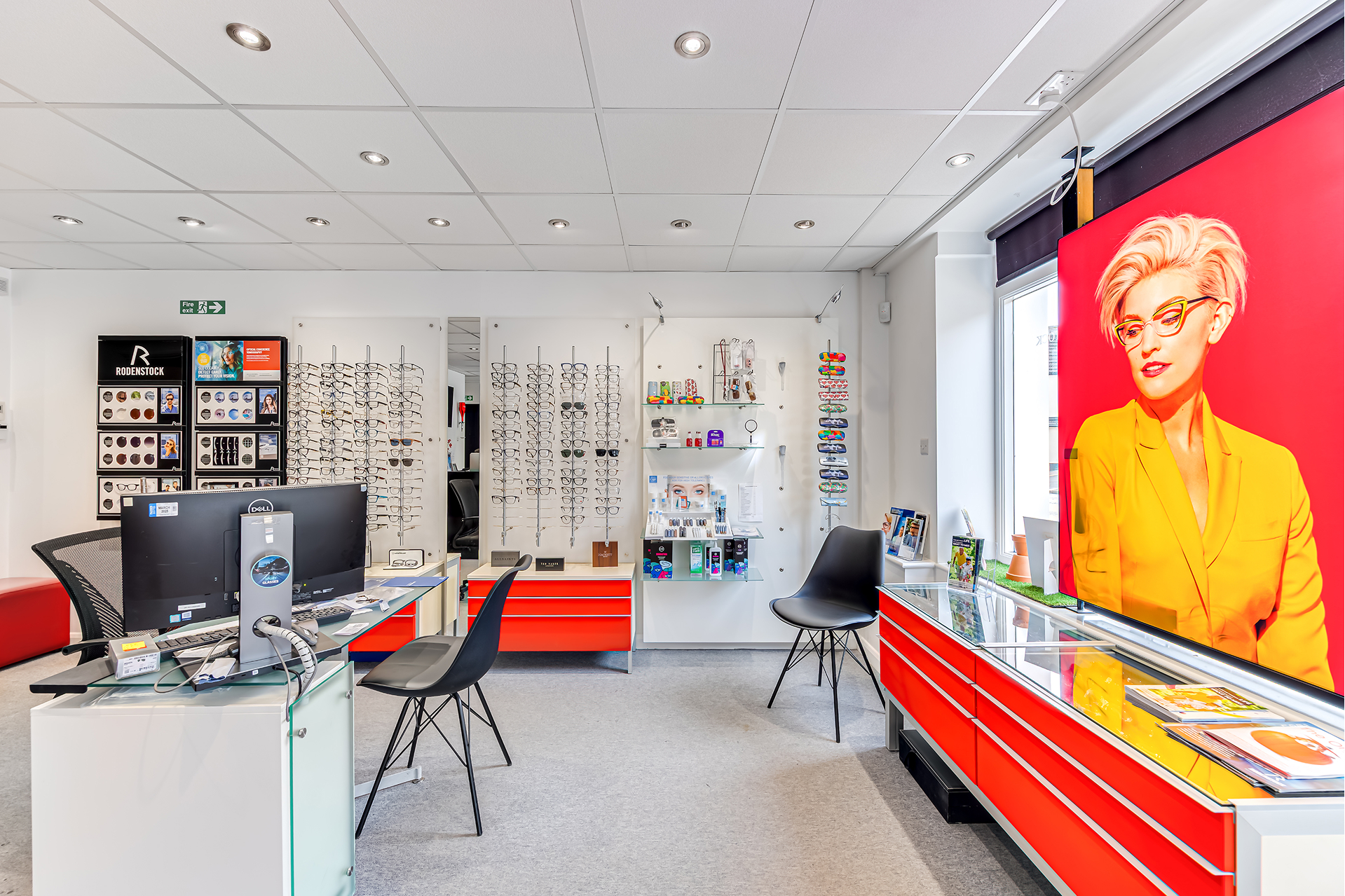 Modern optometry store interior with eyeglass displays, red and black furniture, and pop art portrait