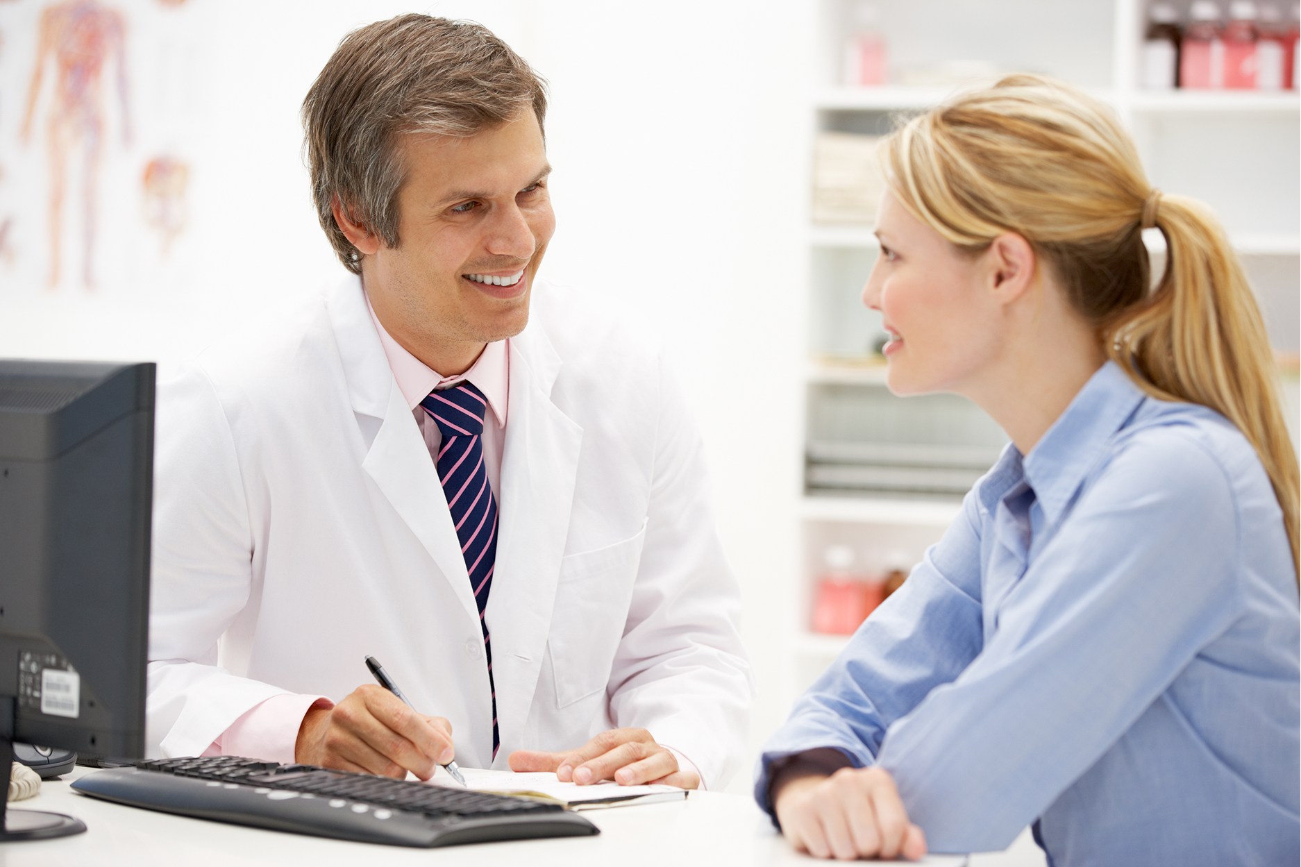 Doctor in white coat smiling while talking with female patient in medical office