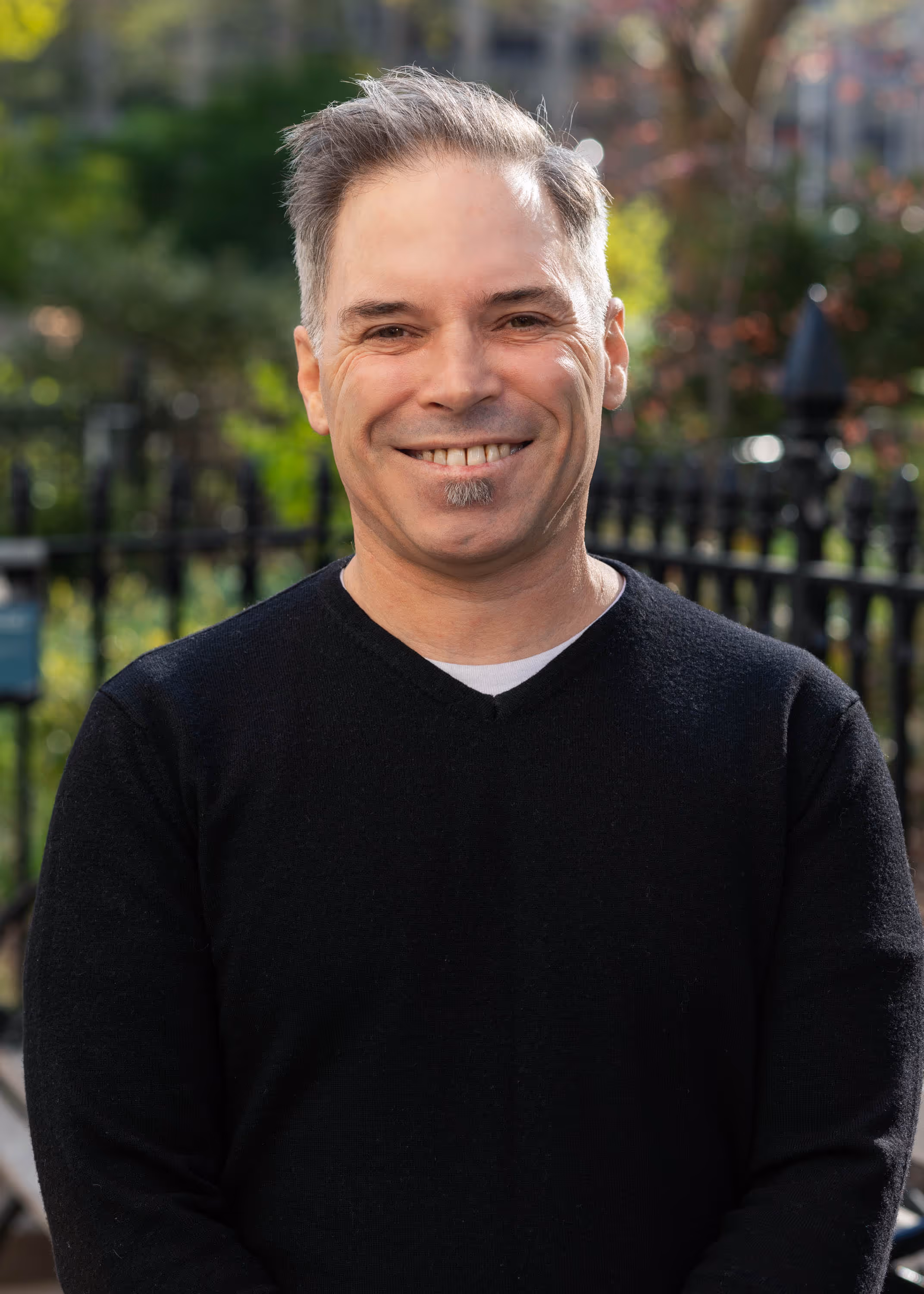 Smiling IT professional in black sweater standing outdoors near iron fence in New York City