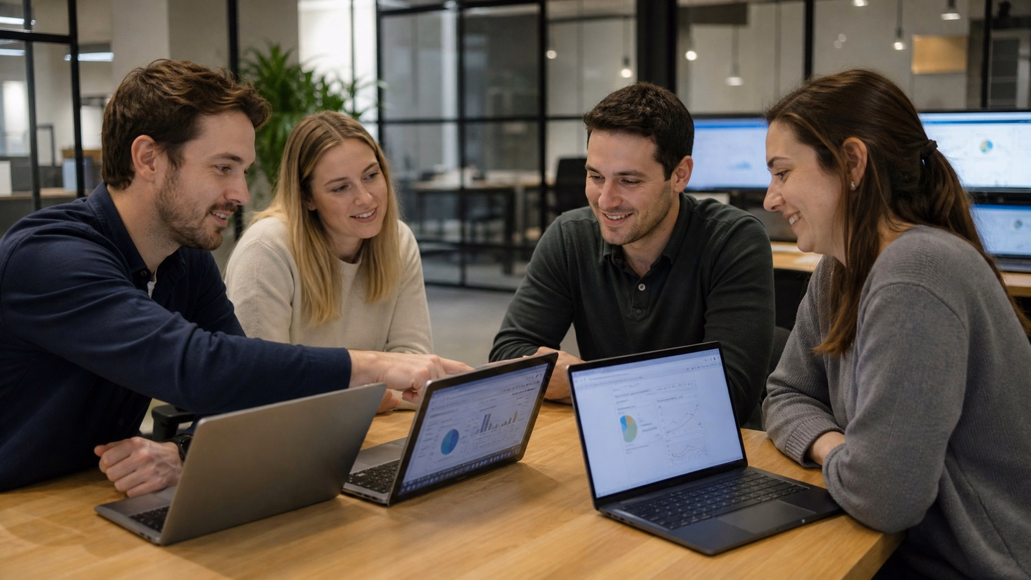 Team collaborates around laptops at table, discussing JAMF