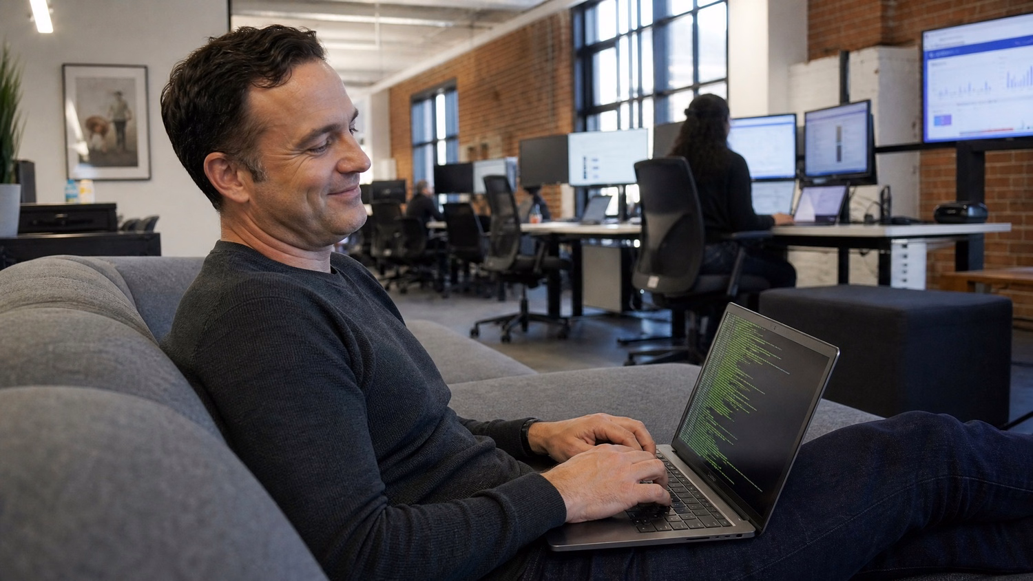 Man working on laptop in office lounge, terminal screen visible
