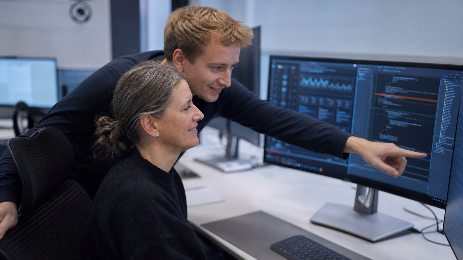 Mentor guiding woman reviewing code on monitor 56 chars