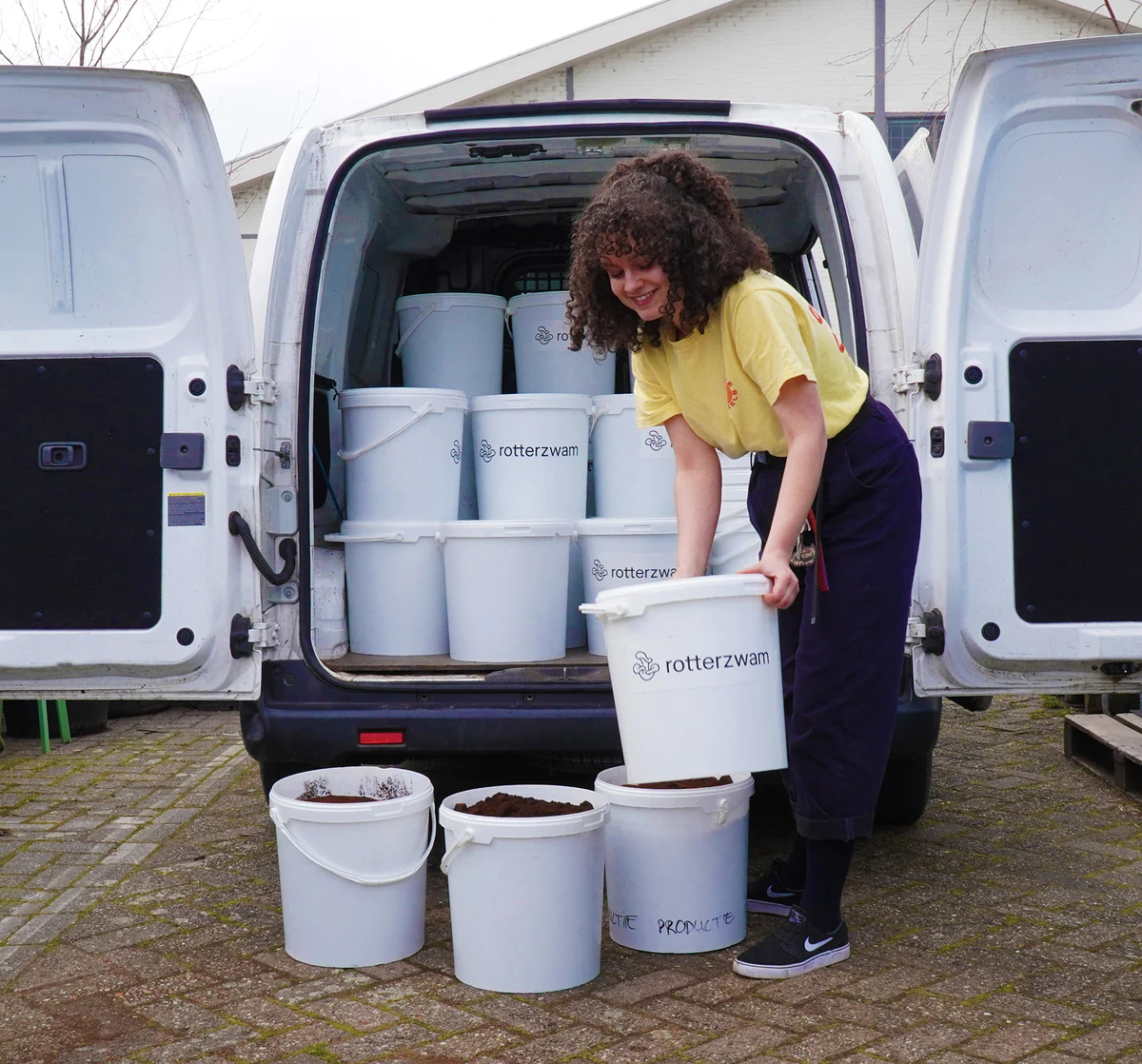 A smiling woman unloading buckets with coffee grounds