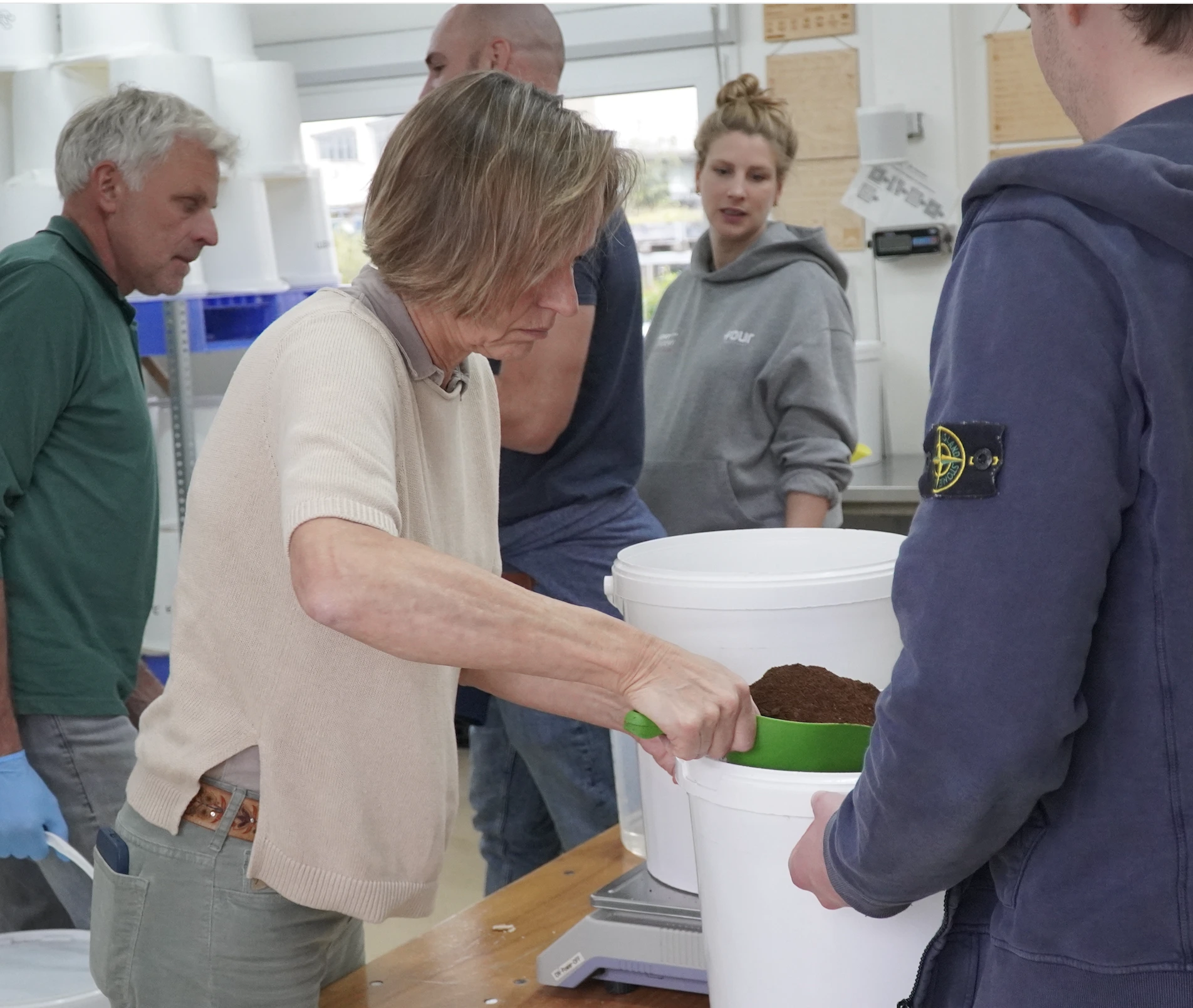 People working together indoors scooping coffee grounds into large white buckets.