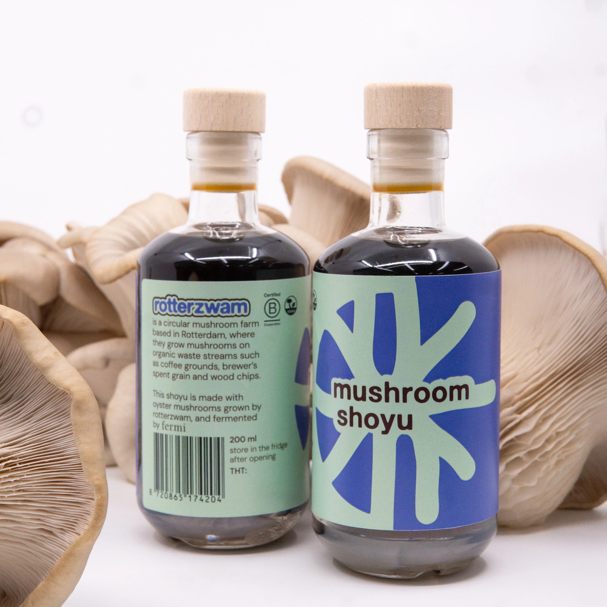 Two bottles of mushroom shoyu with wooden caps surrounded by oyster mushrooms.