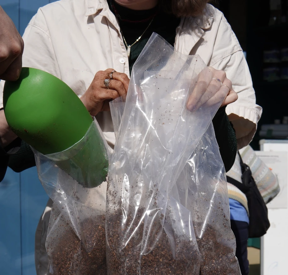 Group of people working outside near a building, handling white plastic bags filled with coffee grounds mix.