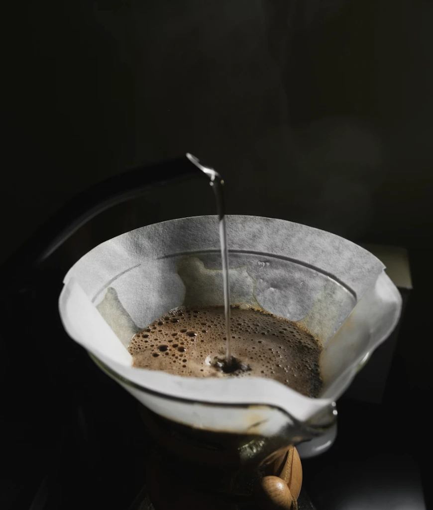 Hot water being poured from a gooseneck kettle into a coffee filter with brewing coffee grounds.