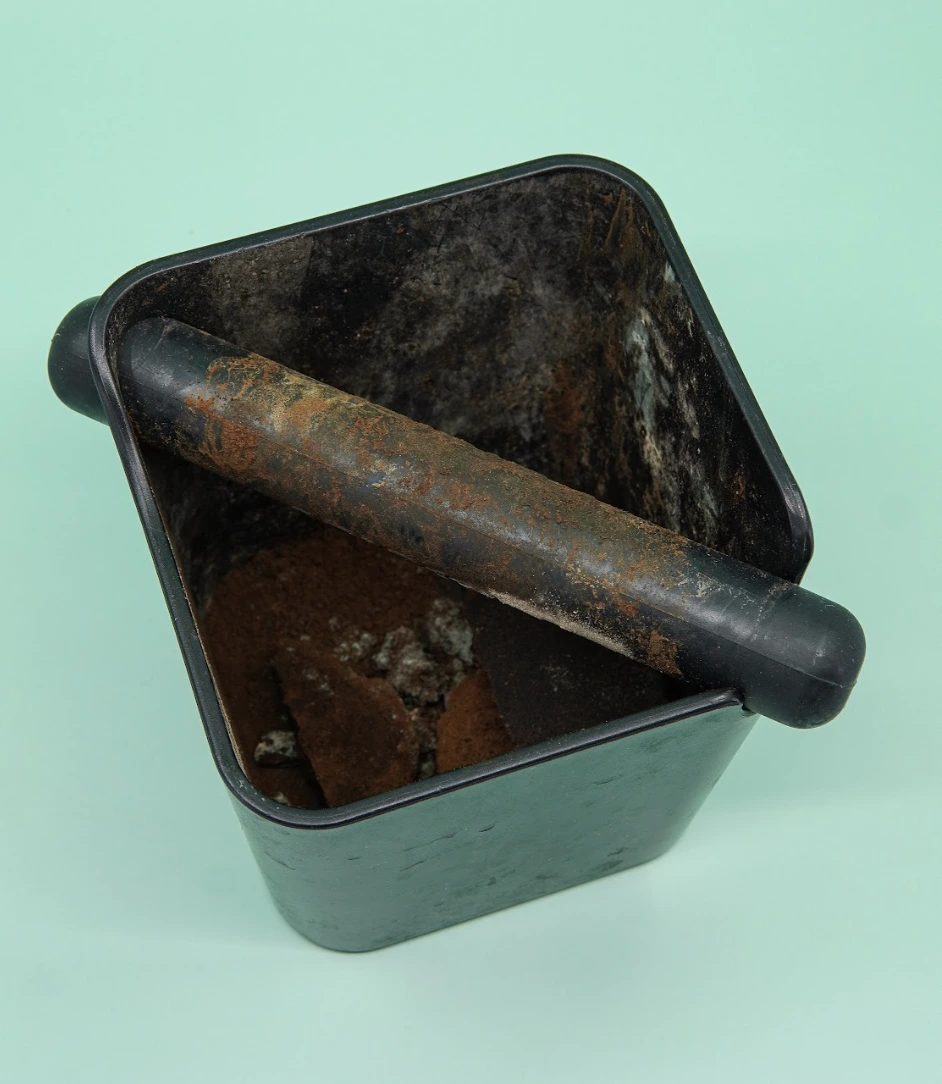 Black container with rusted metal bar and pieces of brown, moldy substance inside.