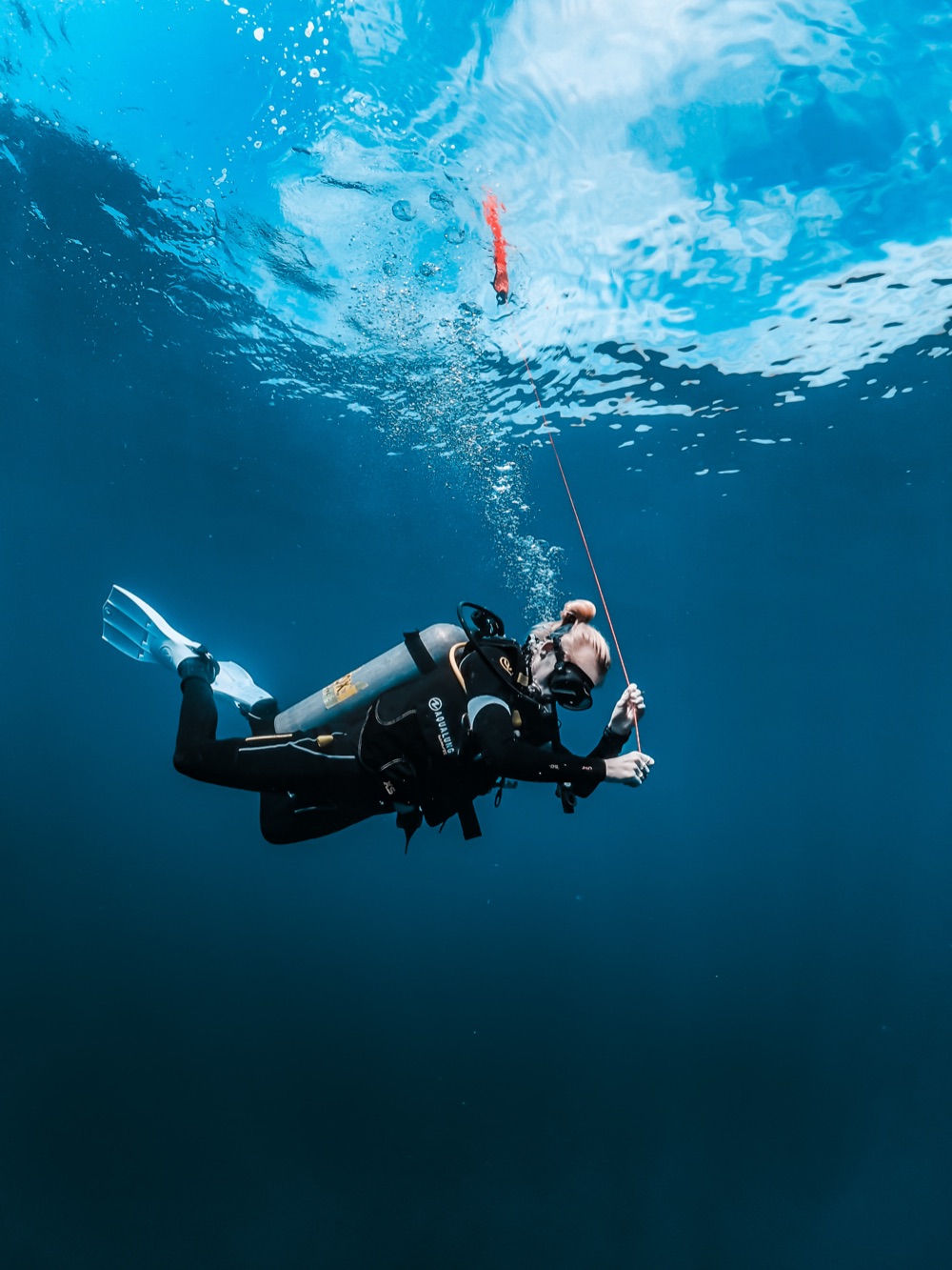 Lucienne underwater in full scuba kit, sending a surface marker buoy up on its reel