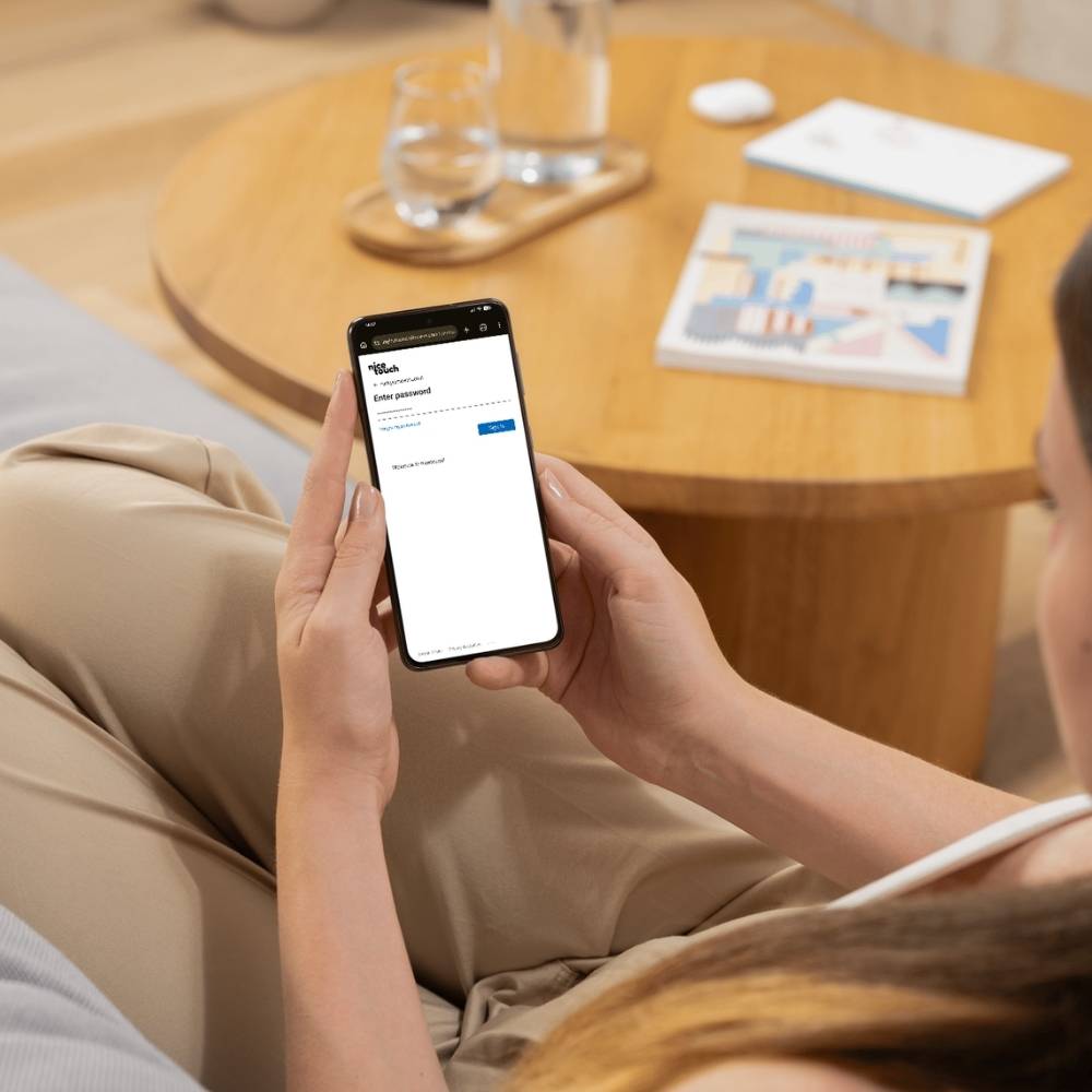 Person sitting on a couch holding a smartphone displaying a password entry screen for a website.