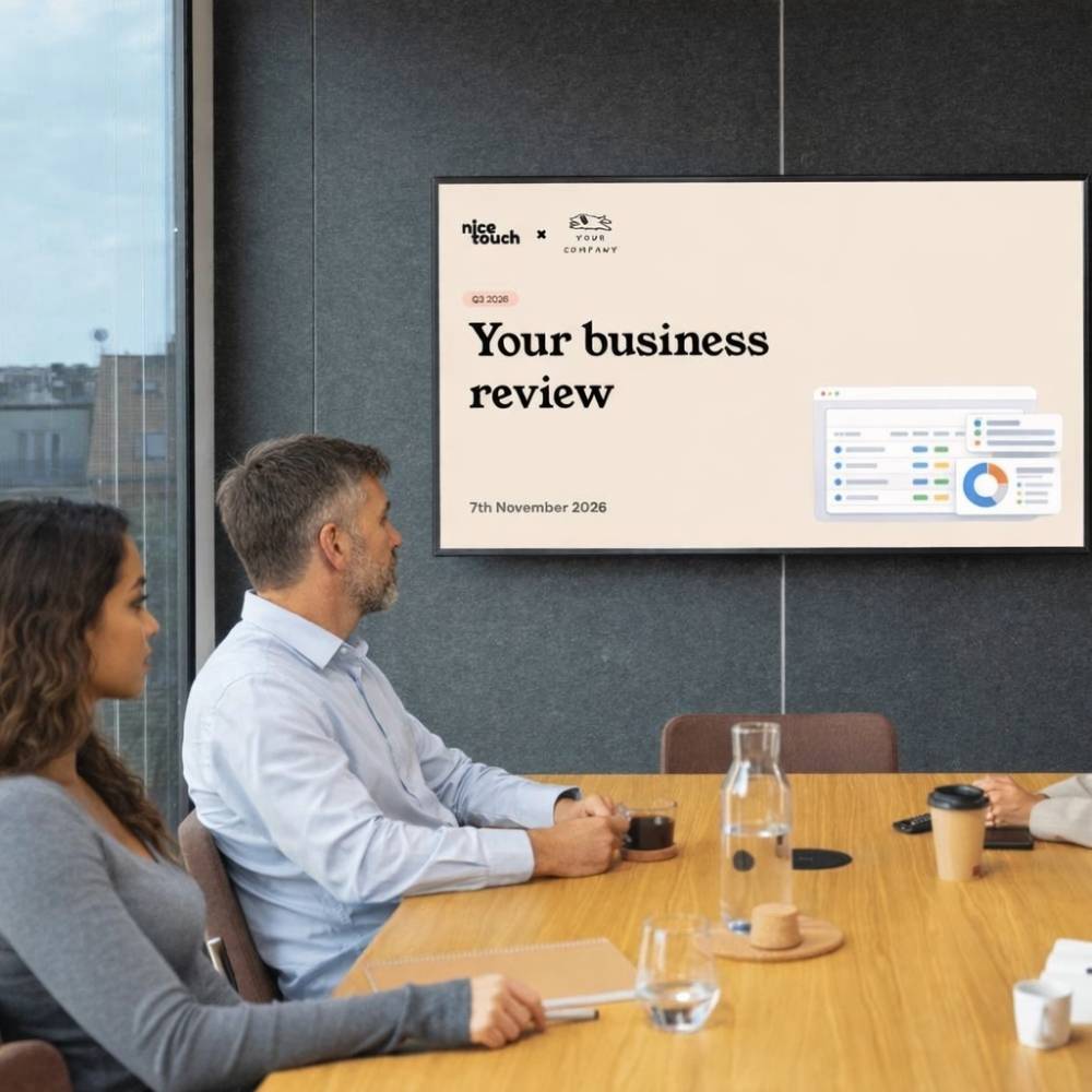 Man standing and pointing at a presentation screen showing a business review while another man sits at a table watching.
