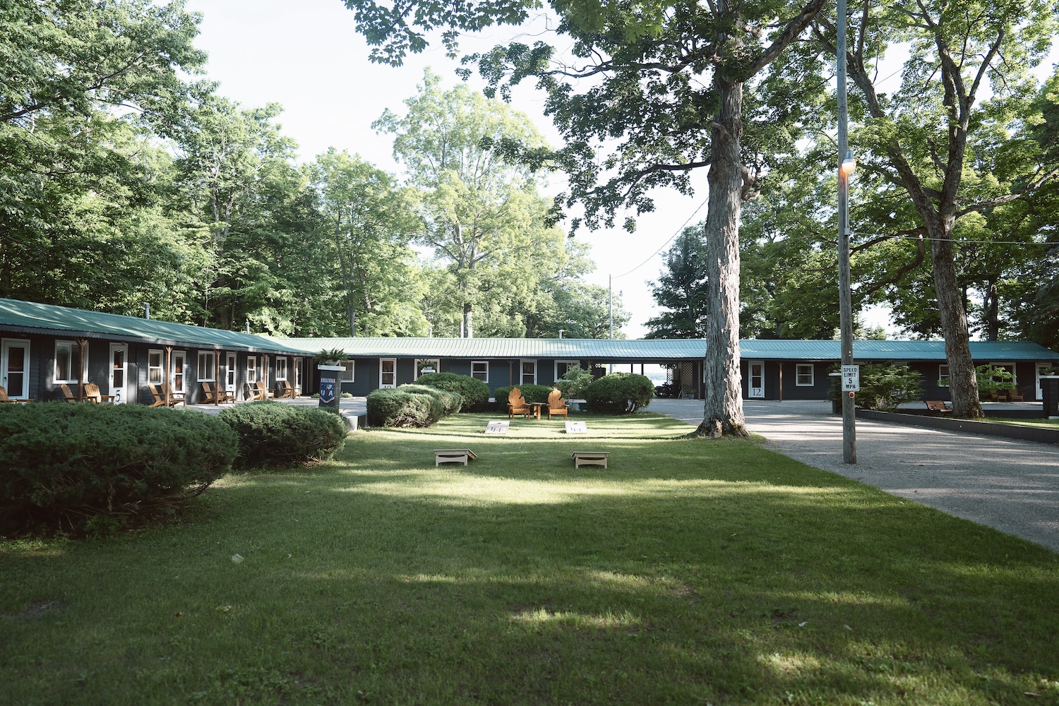 Outdoor view of a motel with green roofs, surrounded by trees and lawns with Adirondack chairs.