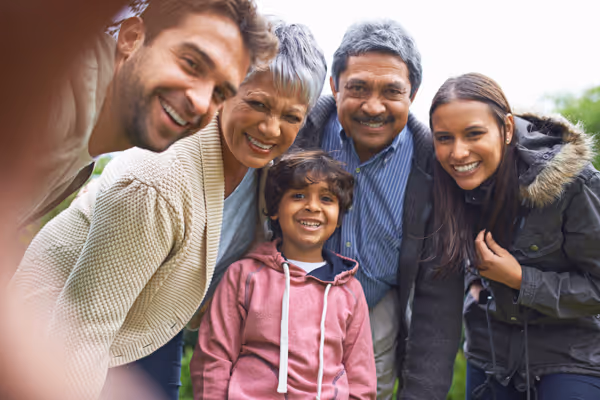 Smiling multigenerational family of five posing outdoors, looking into the camera.
