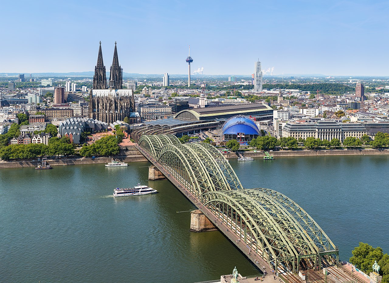 Luftaufnahme vom Kölner Dom, der Hohenzollernbrücke und dem Rhein bei klarem Himmel.