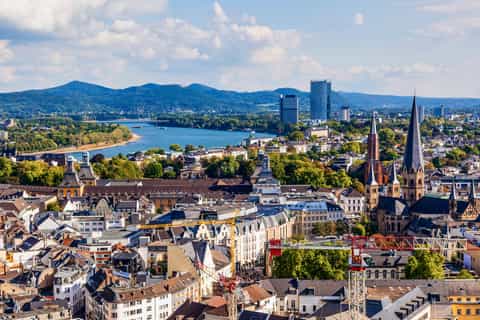 Blick auf Bonns Stadtzentrum mit Rhein, Kirchtürmen und umliegenden Hügeln bei klarem Himmel.
