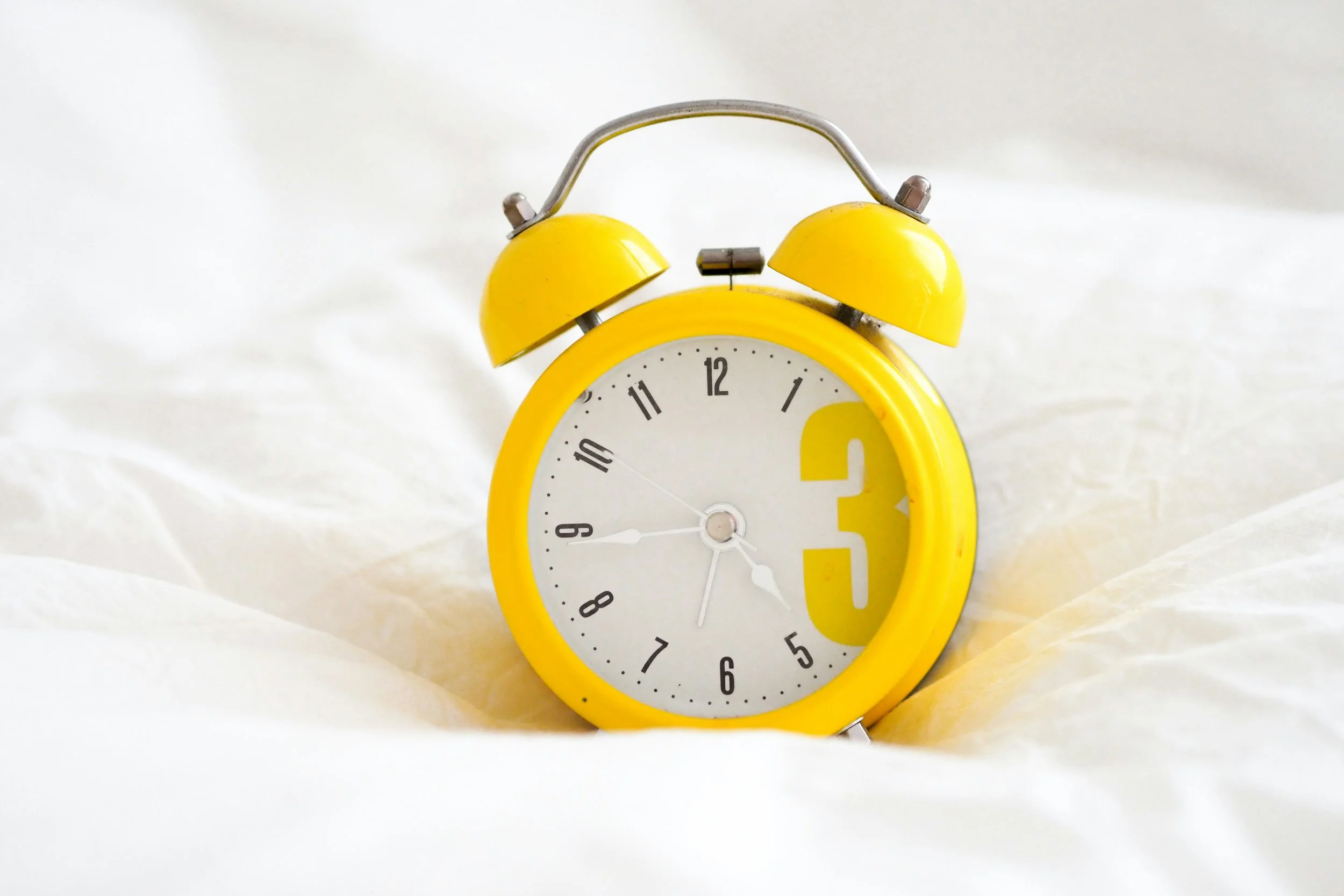 yellow alarm clock on white bedding