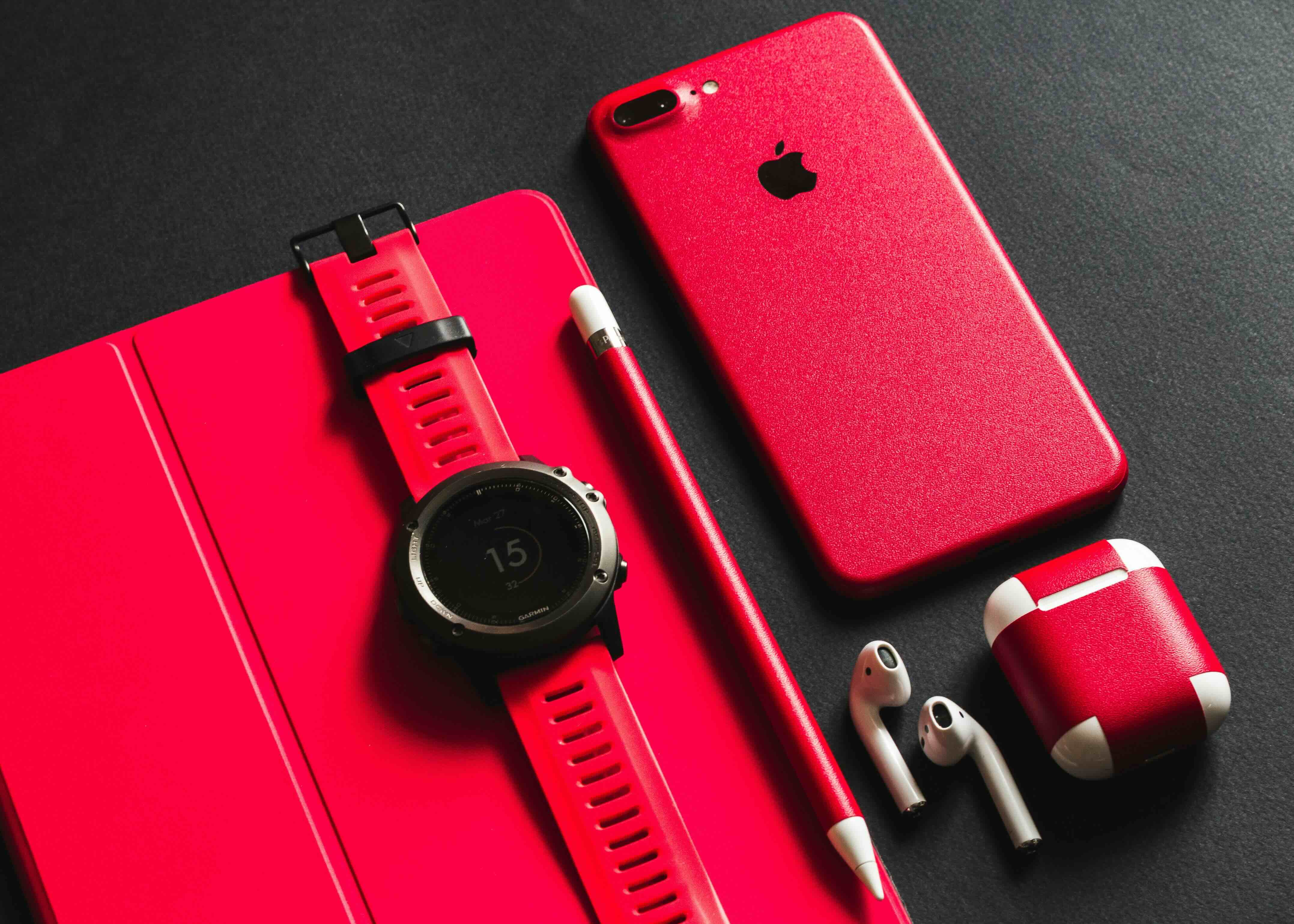 Wearables, iphone, planner, headphones all in red on a productive desk
