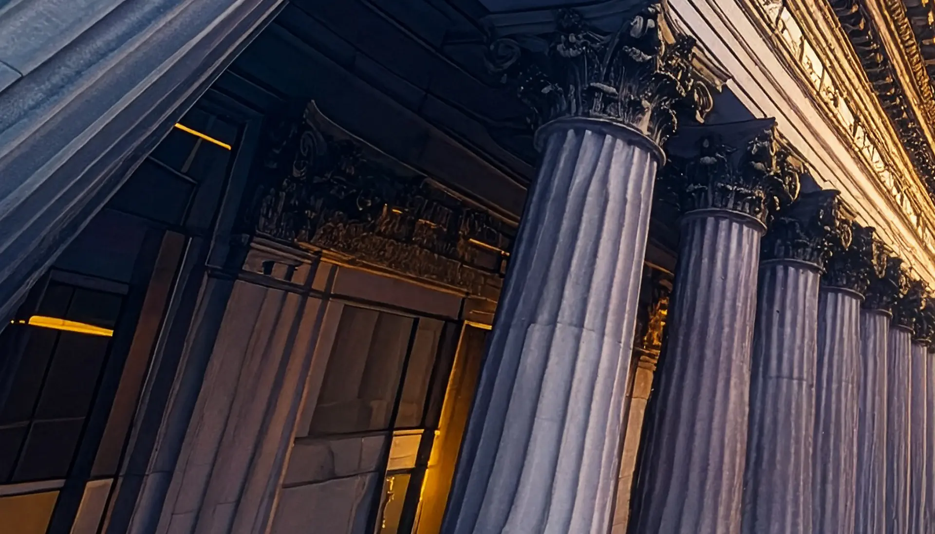 Close-up of classical stone columns with Corinthian capitals on a historic building illuminated by warm light.