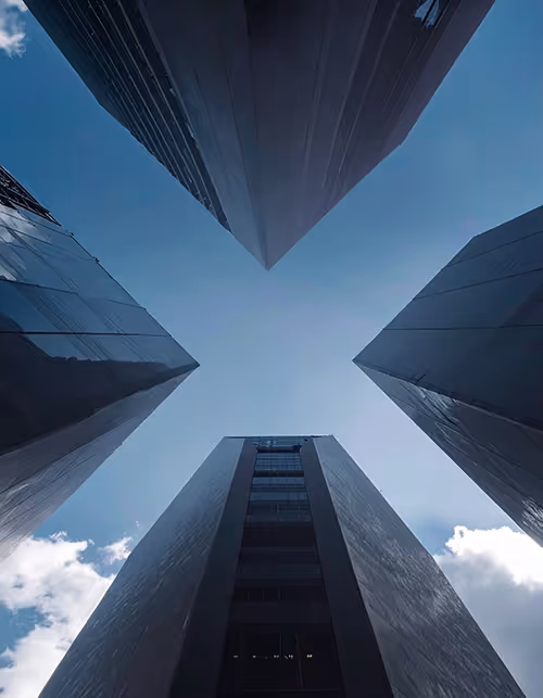 View looking up at four tall modern skyscrapers forming a cross shape against a blue sky with some clouds.