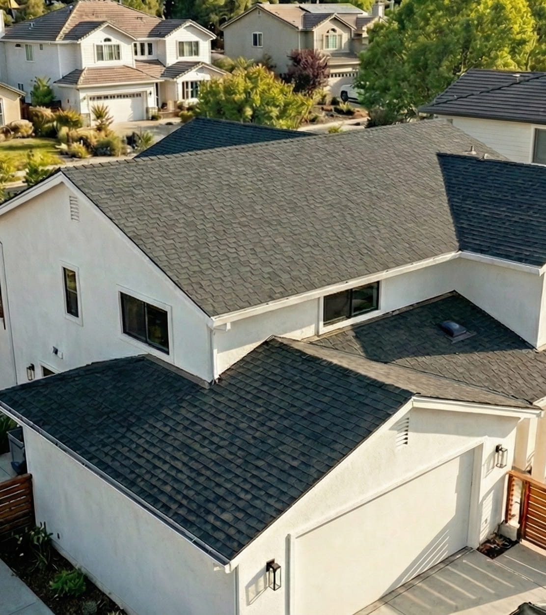 Aerial view of a modern two-story house with light-colored exterior walls and dark shingled roof in a suburban neighborhood.