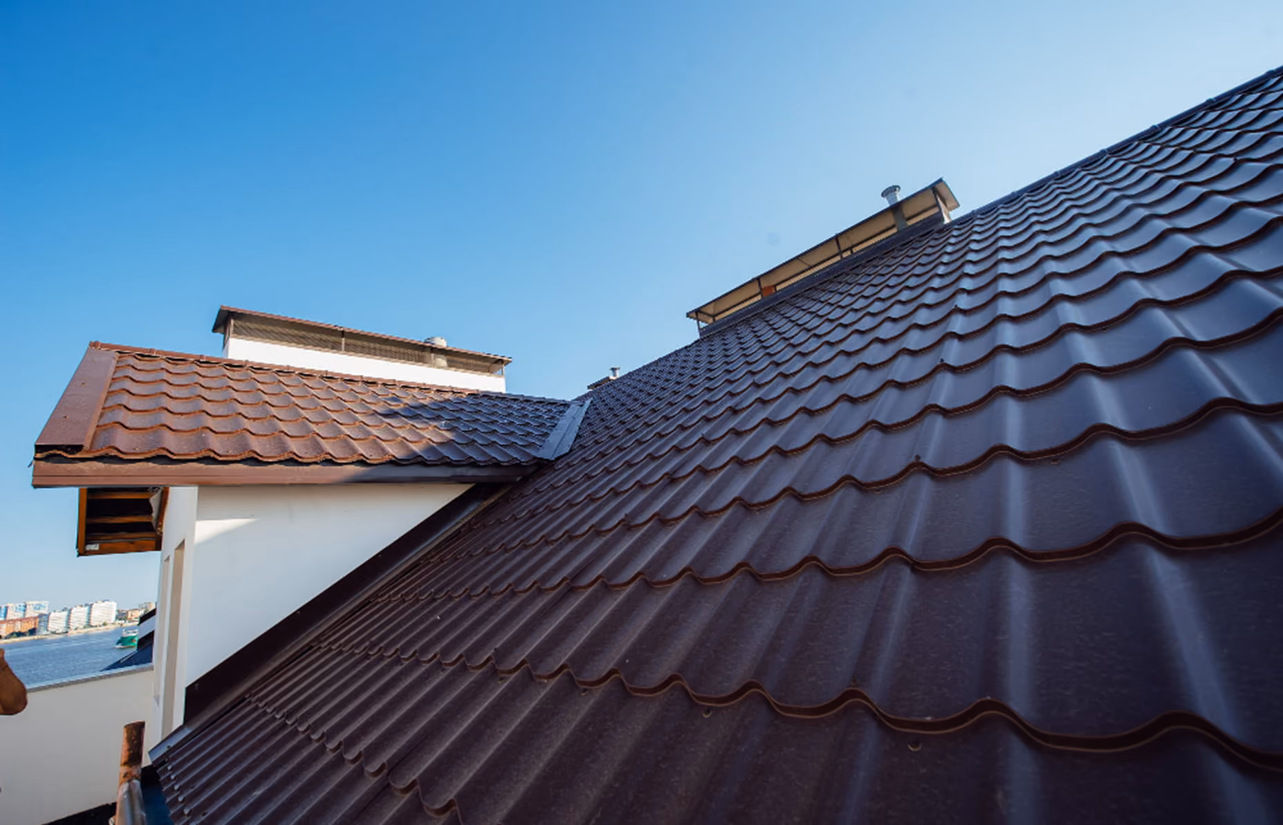 Close-up view of a brown metal tiled roof with a clear blue sky in the background.