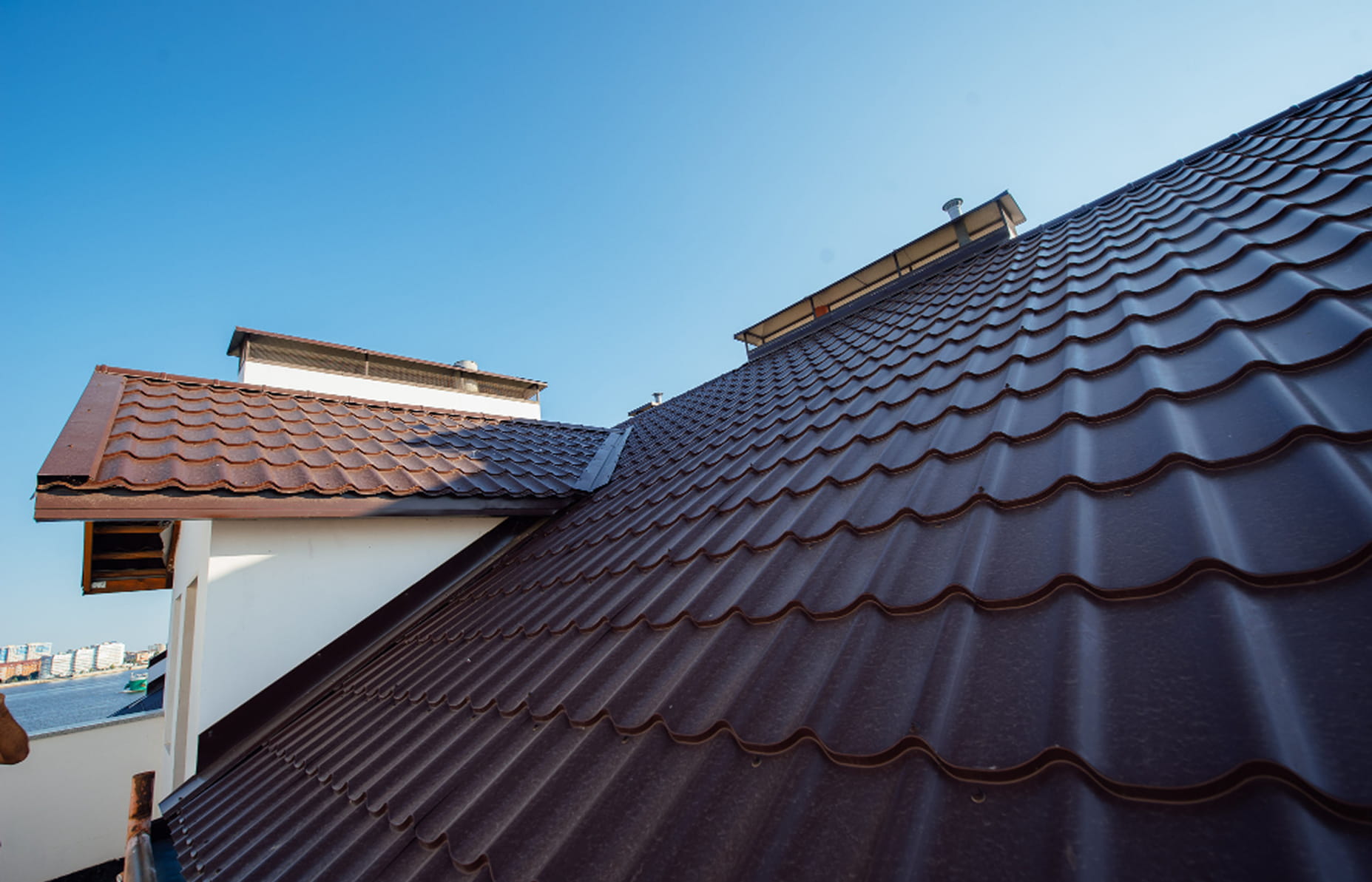 Close-up view of a brown metal tiled roof with a clear blue sky in the background.