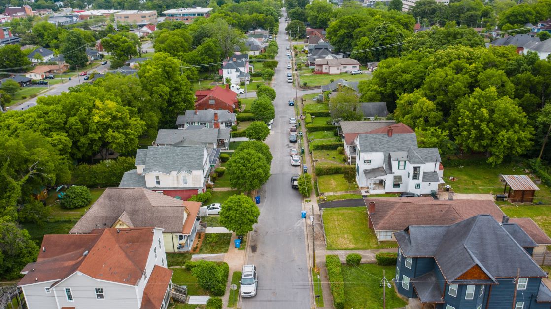 Drone shot showcasing a charming residential area with houses, trees, and parked vehicles
