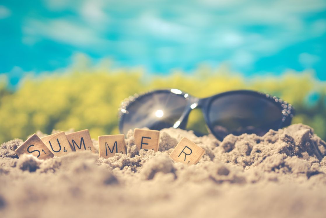 image of sunglasses in the sand with tiles spelled summer