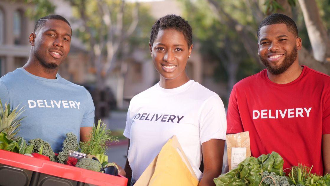Smiling delivery team carrying fresh groceries and packages outdoors
