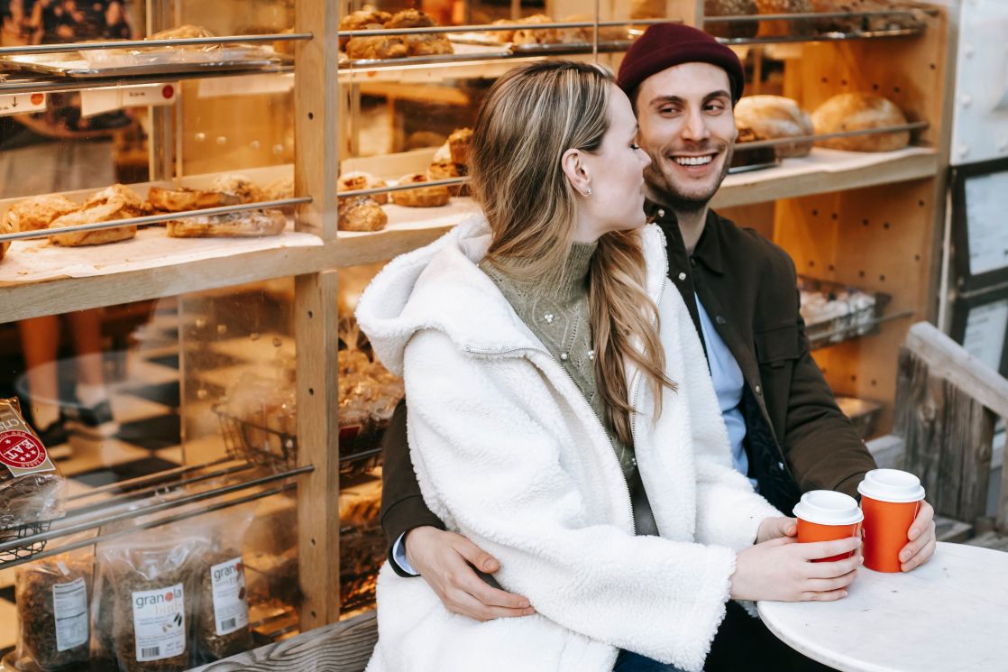 Happy couple enjoying a cozy coffee date outside a bakery with warm drinks.