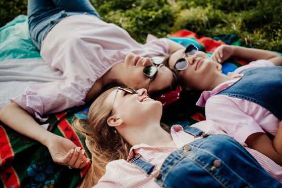 Three women enjoying a sunny day relaxing on a picnic blanket in the park.
