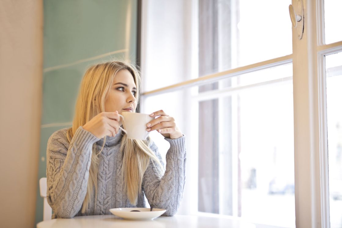 A woman with blonde hair enjoys a warm coffee in a cozy indoor cafe setting.
