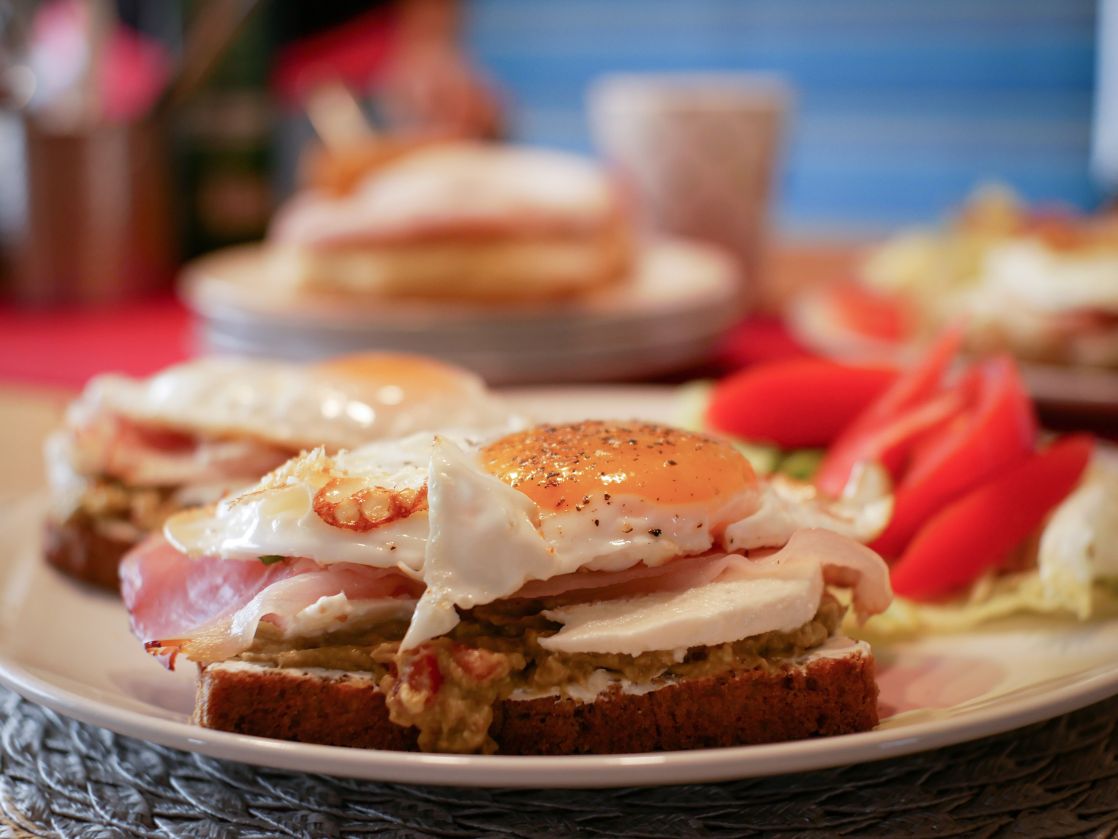Close-up of a savory breakfast with fried eggs, avocado, and ham on toast.