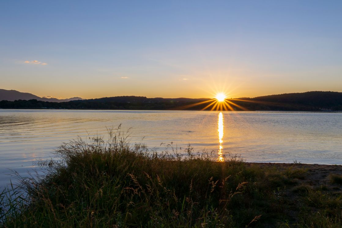 Serene sunset scene capturing a golden sun setting over a calm lake, reflecting on the water.