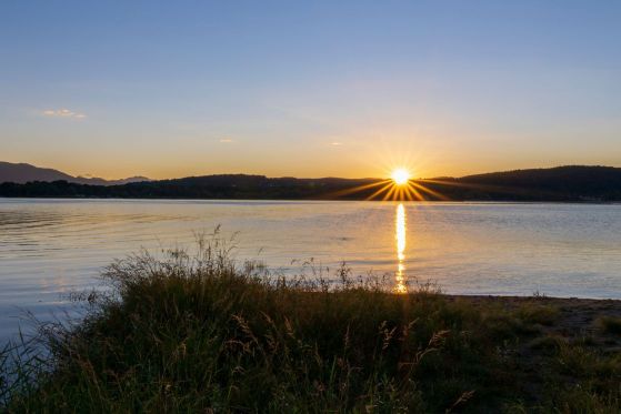 Serene sunset scene capturing a golden sun setting over a calm lake, reflecting on the water.