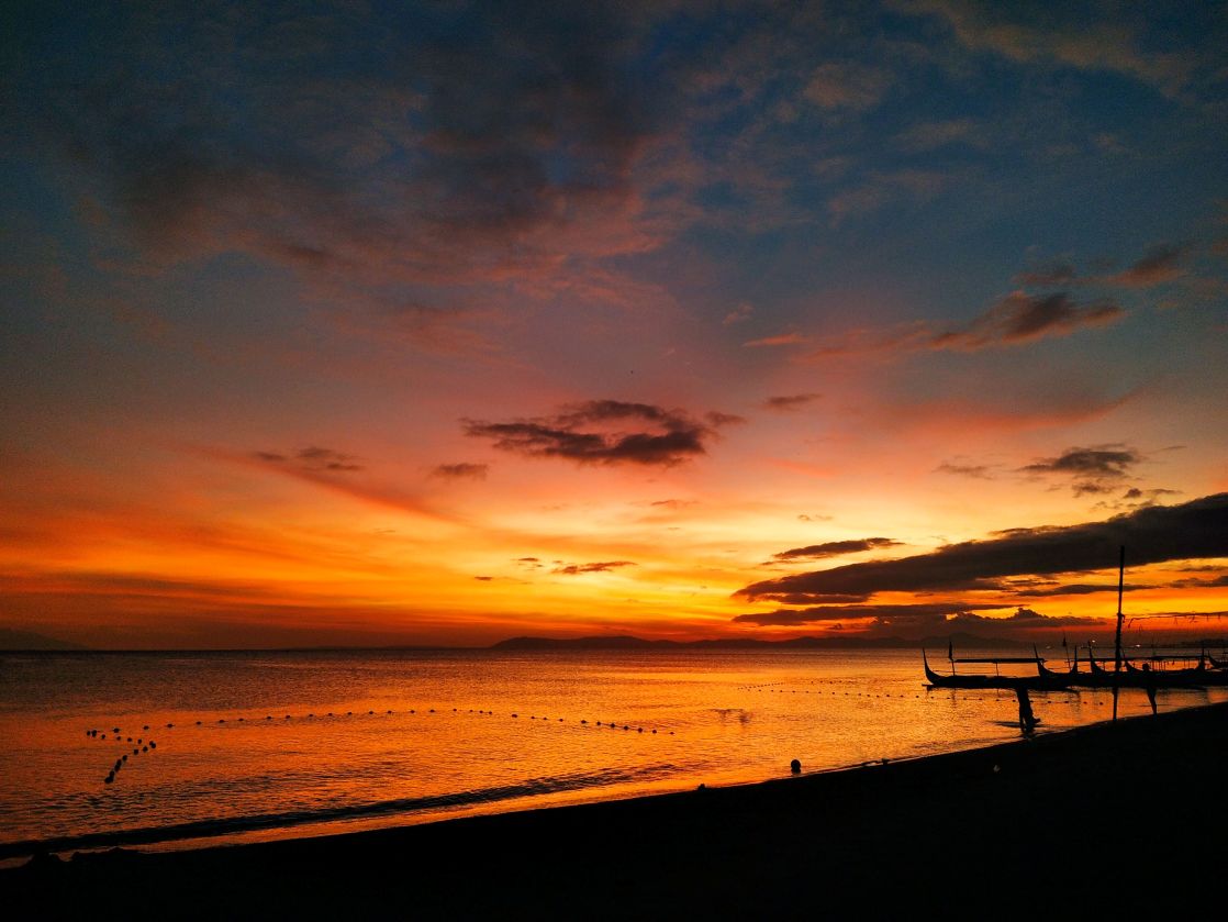 A breathtaking sunset over the beach with silhouettes of boats