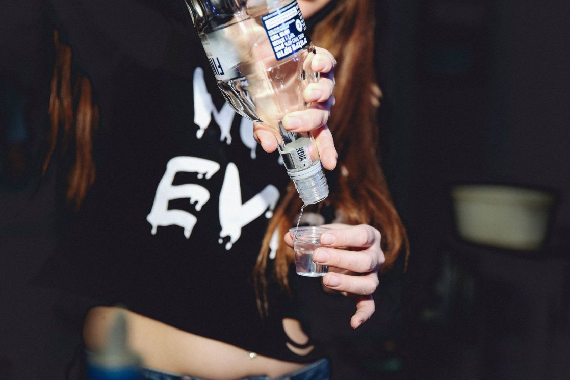 A woman pours vodka into a shot glass during a night gathering, symbolizing nightlife and celebration.