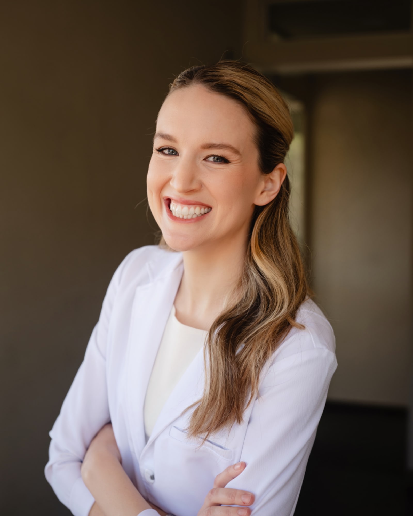Confident female dentist in white coat with arms crossed smiling at camera