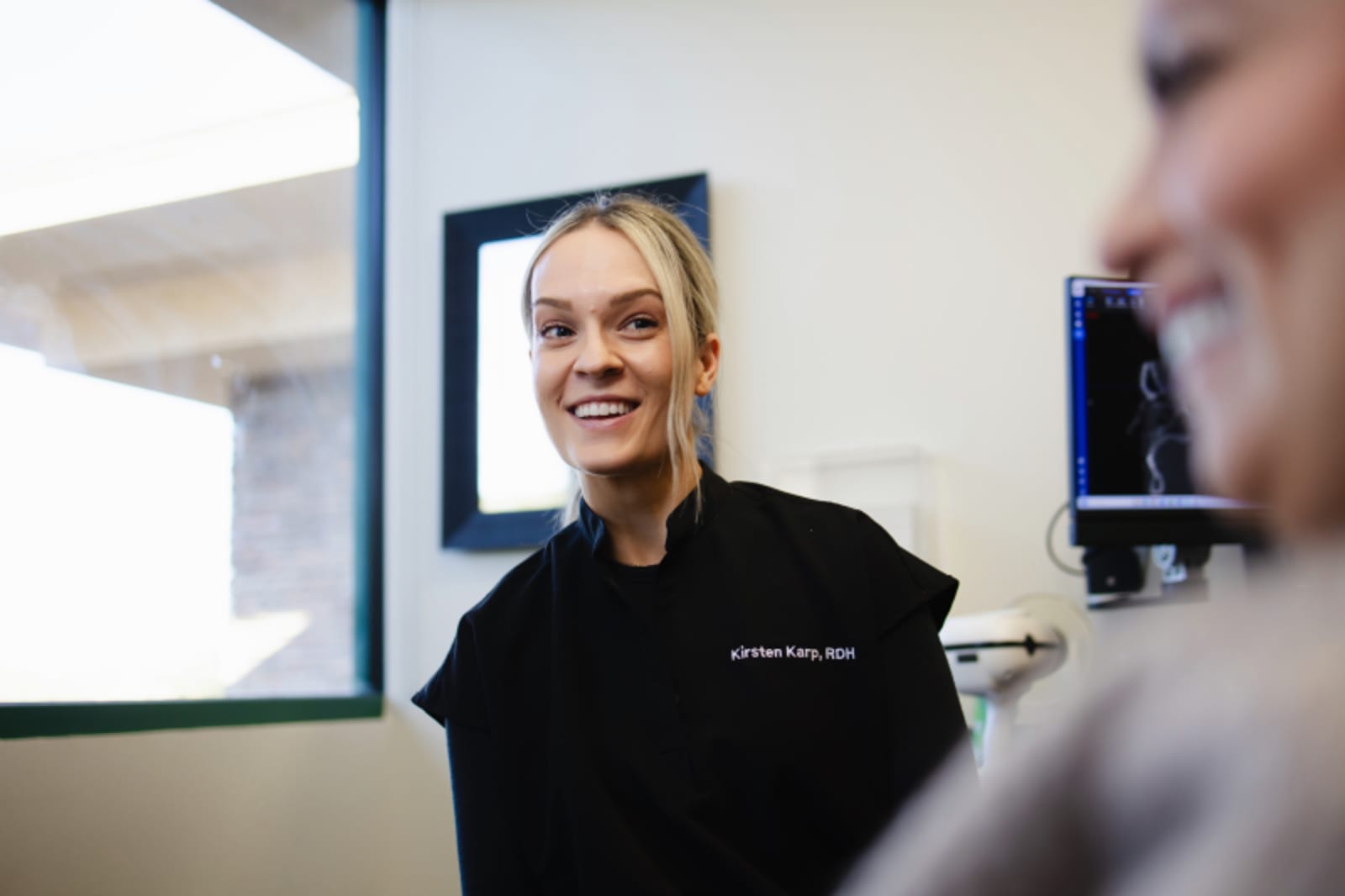 Female dentist smiling during a consultation with a patient in a modern dental office treatment room.