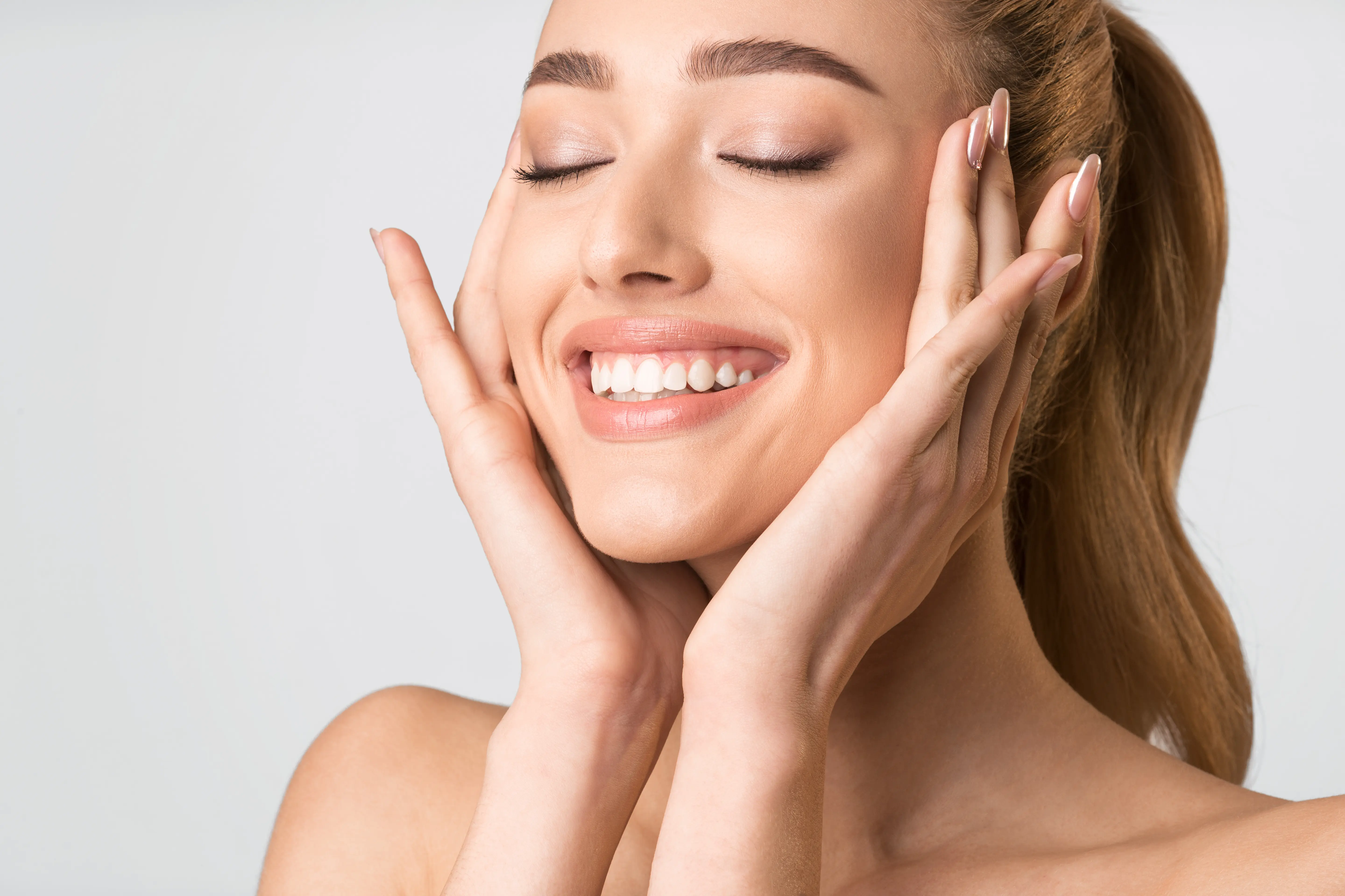 A woman smiling with her hands on her face.