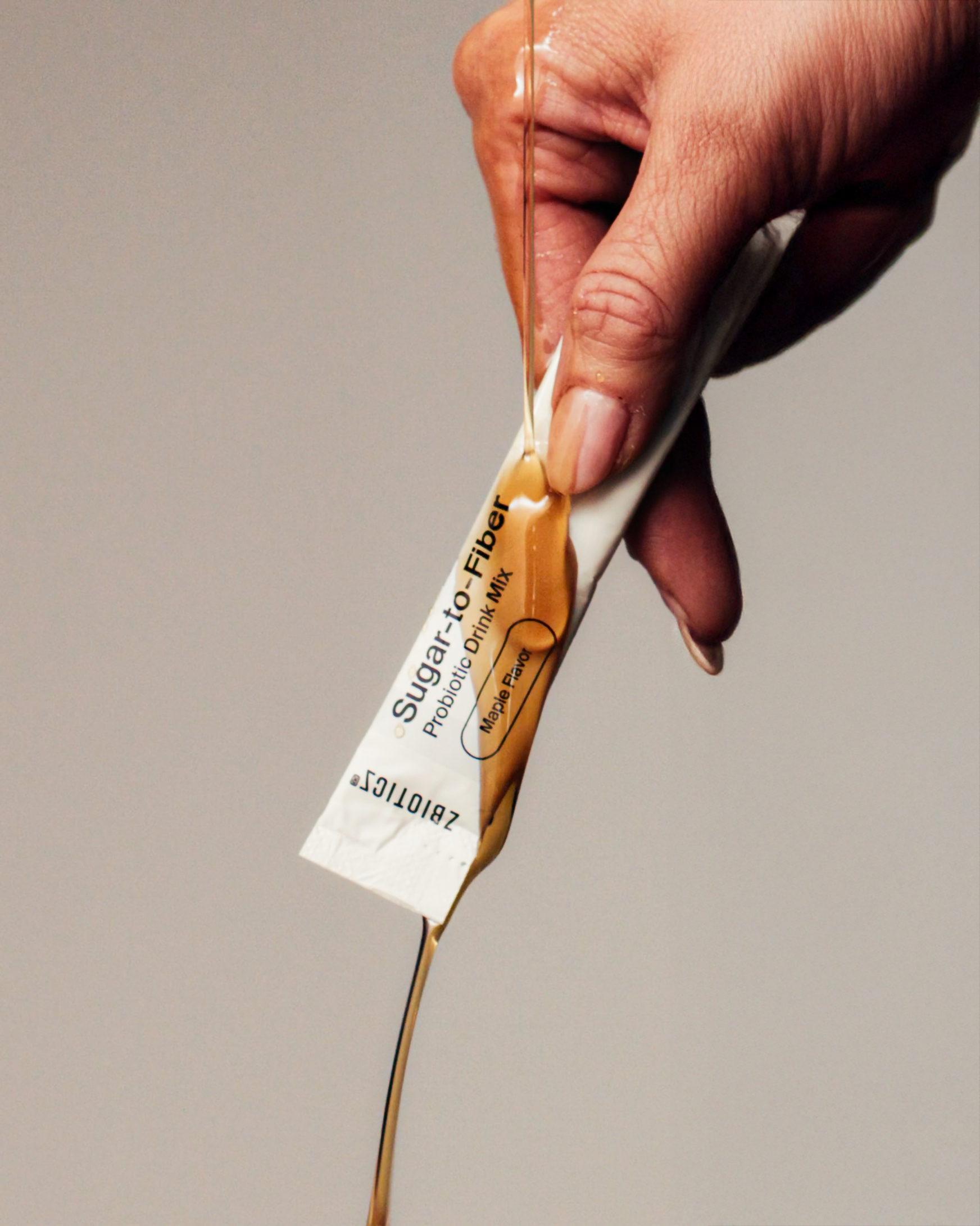 Hand squeezing a Sugar-to-Fiber Probiotic Drink Mix packet, labeled maple flavor, with liquid pouring out.