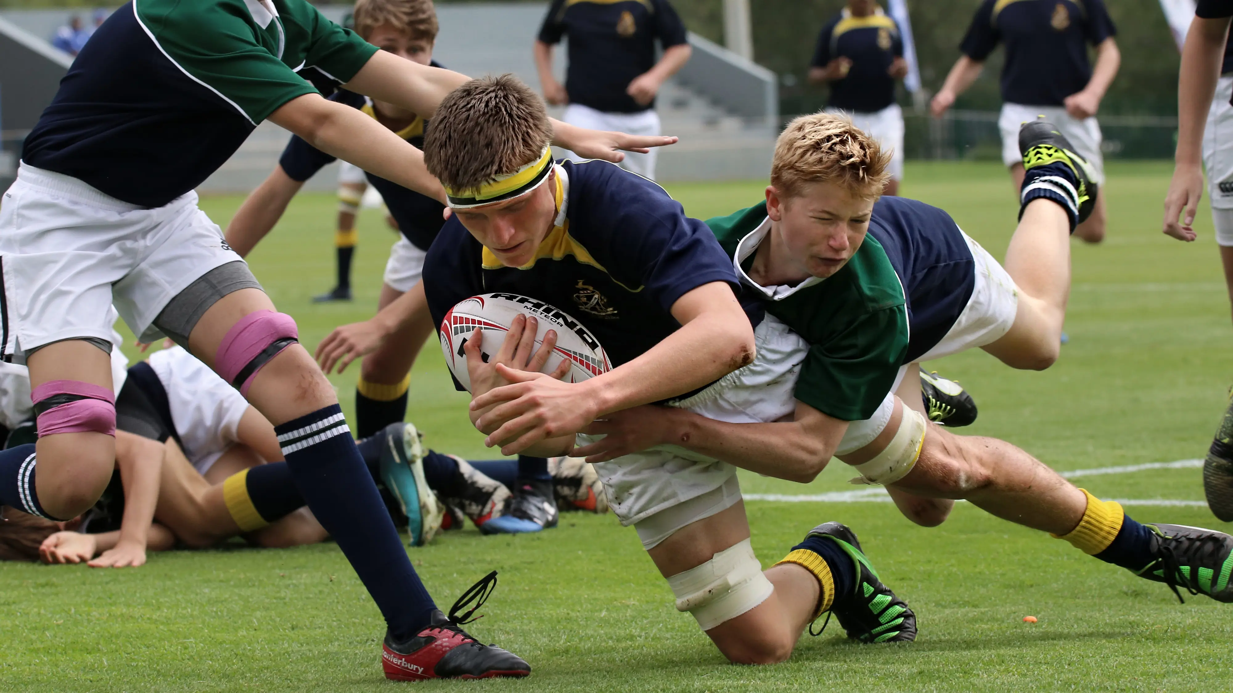 Two rugby players in mid-tackle during a match, one holding the ball and the other attempting to stop him.