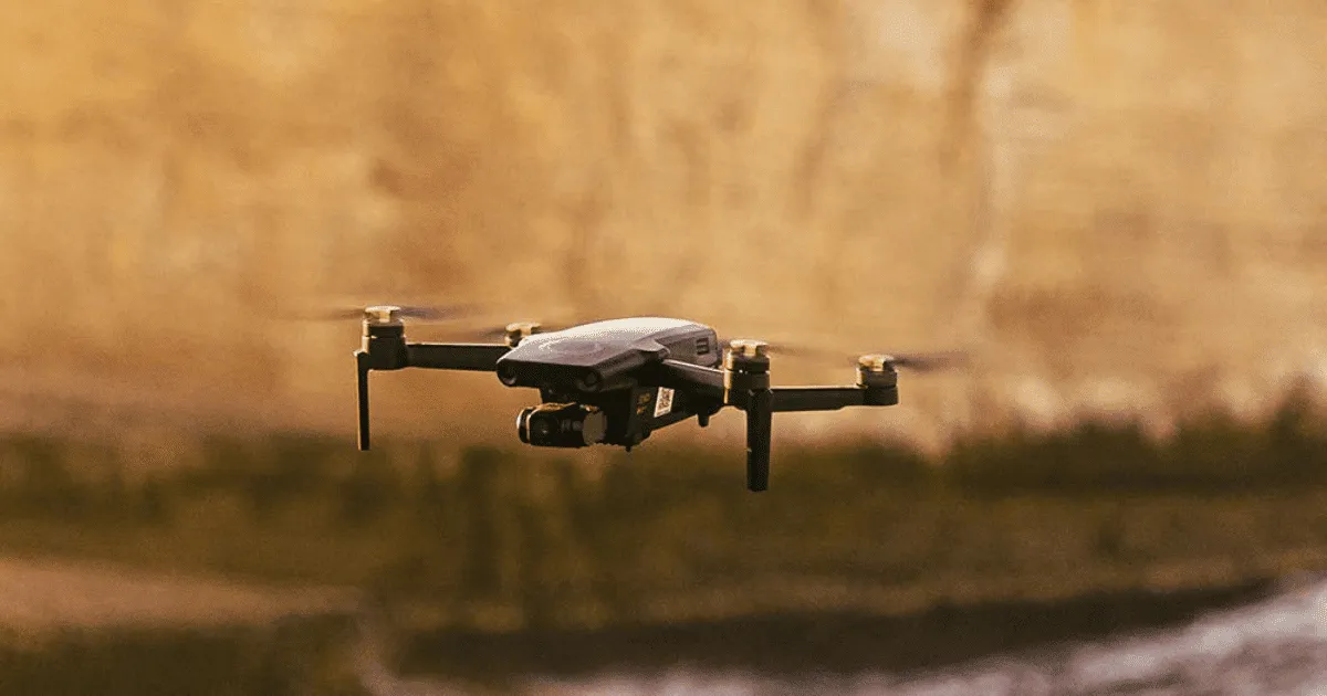 Compact black drone with four propellers flying outdoors against a blurred background.