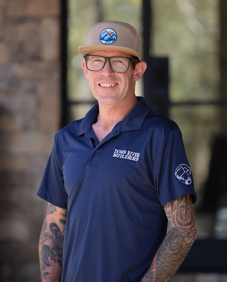 Owner wearing glasses, a beige cap with a Down River Builders logo, and a navy blue polo shirt with Down River Builders logo.