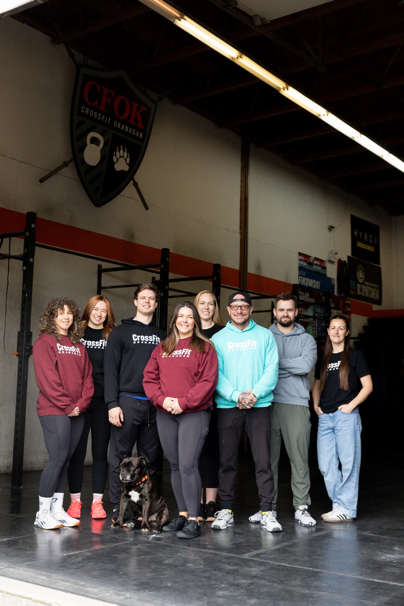 Group of eight CFOK coaches and a Murph the dog standing inside the CrossFit gym under a CFOK CrossFit Okanagan sign.