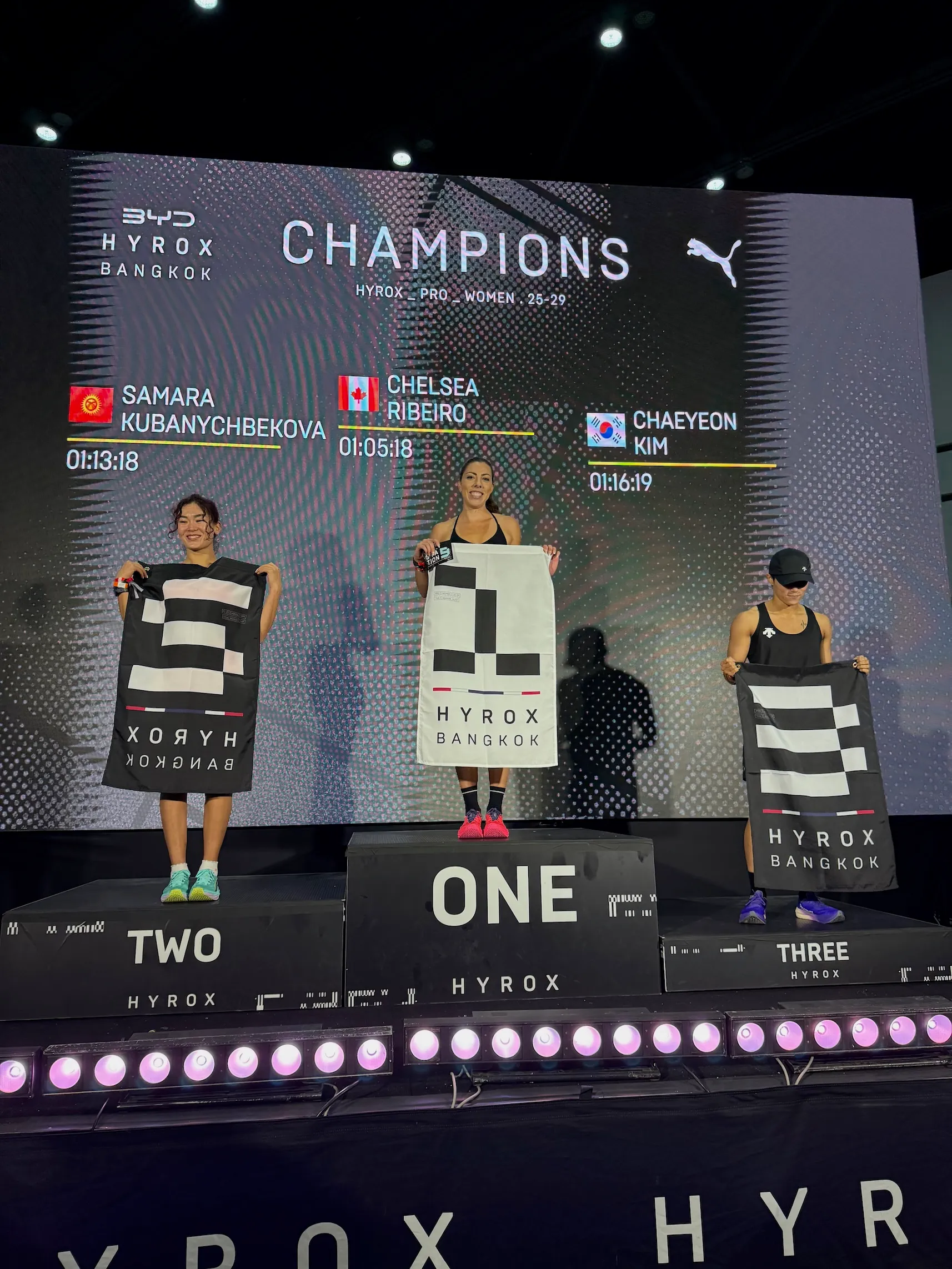 Chelsea Ribeiro standing on top of the podium after winning a HYROX race.