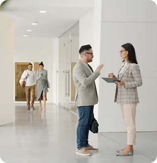 Two people standing and talking in a bright hallway while two others walk in the background.