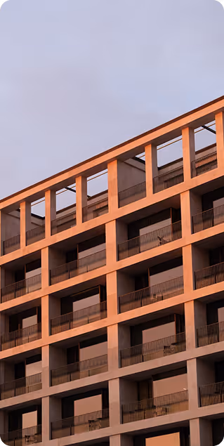 Modern building facade with multiple balconies and rectangular frames bathed in warm, orange sunlight against a cloudy sky.